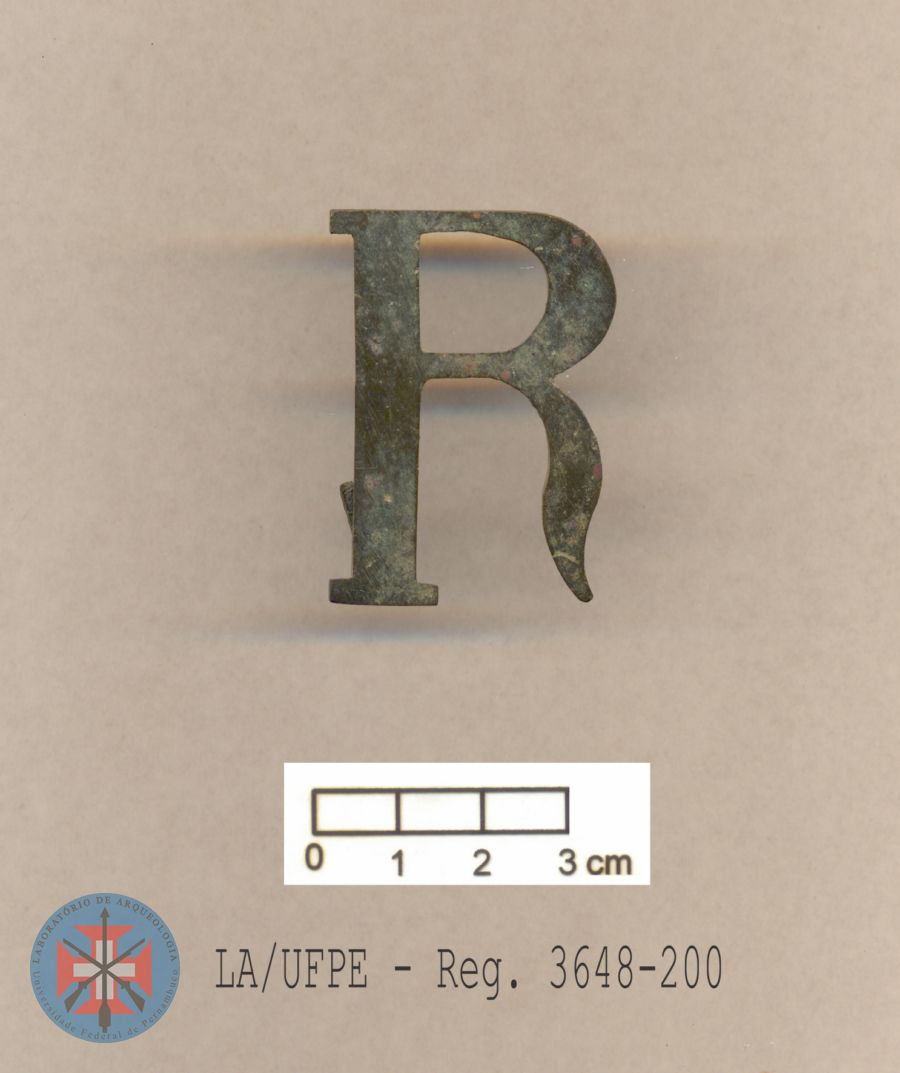 Peça na forma de letra 'R', em bronze, letra esta normalmente associada ao 'Regimento de Segurança' da polícia republicana, no início do século XX. Possivelmente seria uma insígnia de quepe. Séc. XX. (RA)